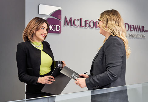Two lawyers smiling in front of the McLeod Green Dewar LLP & Associates sign on the wall